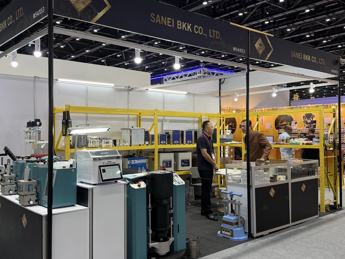 Visitors and the SANEI BKK team talking beside machinery at the Bangkok Gems booth.